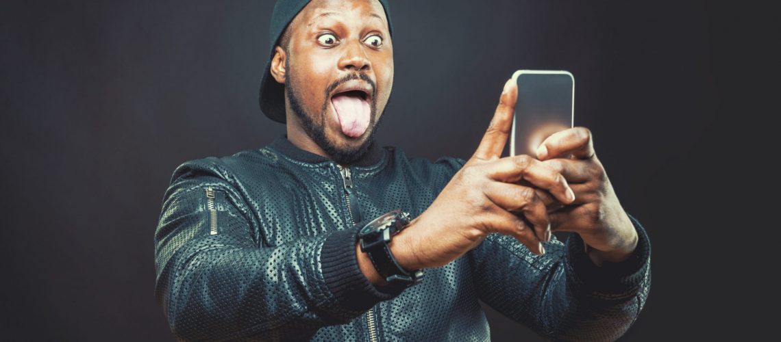 Handsome young man use his smart phone for a funny face selfie shot